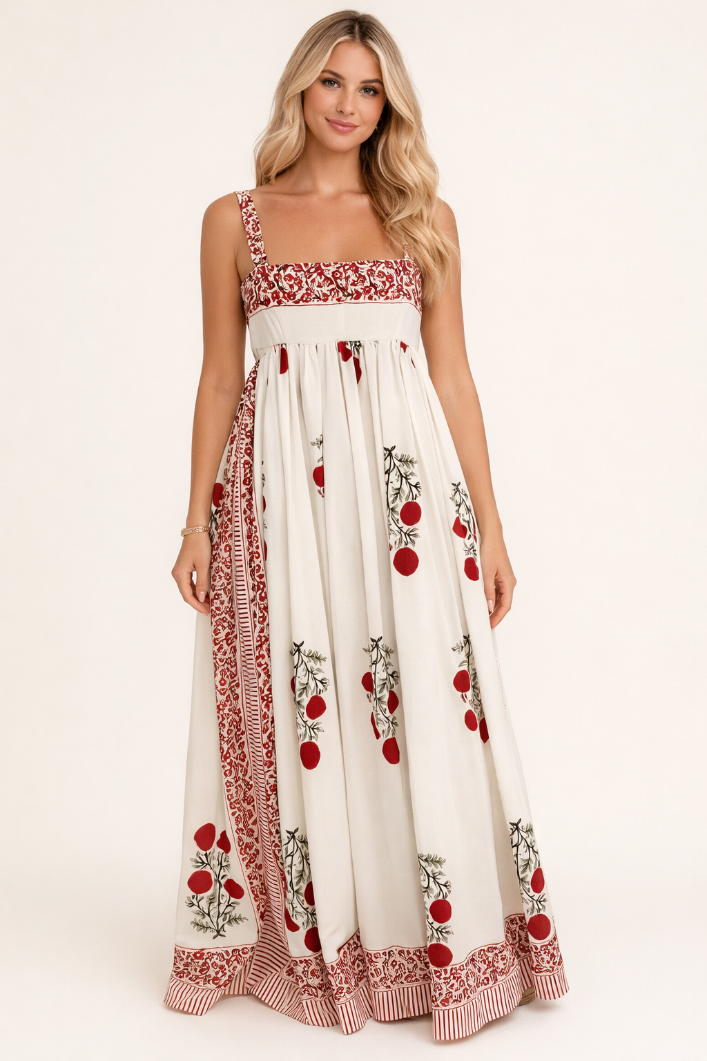Vrouw draagt een crème maxi jurk met rode botanische print en contrasterende sierdetails in een elegante binnenruimte