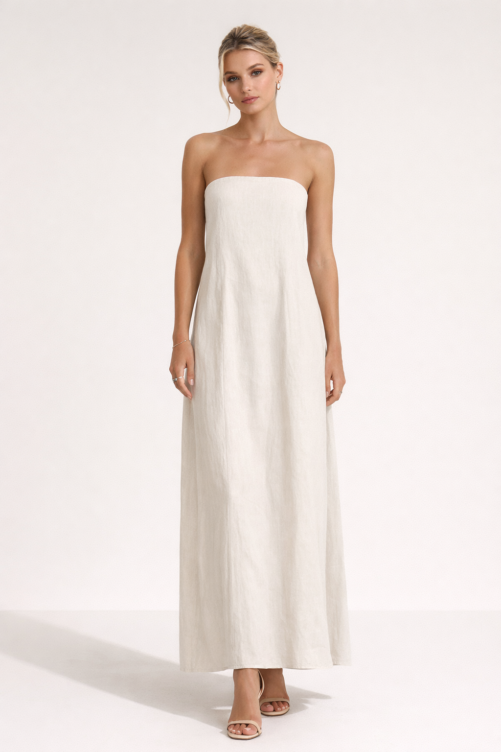 Strapless beige maxi jurk in minimalistisch design gedragen met kleine handtas