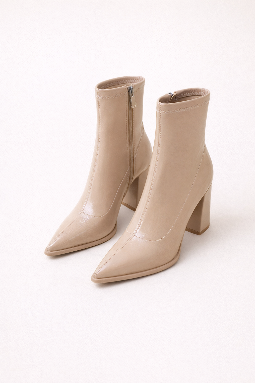 Beige enkellaarsjes met puntige neus en hak, elegante dameslaarzen op een vintage krantenachtergrond.