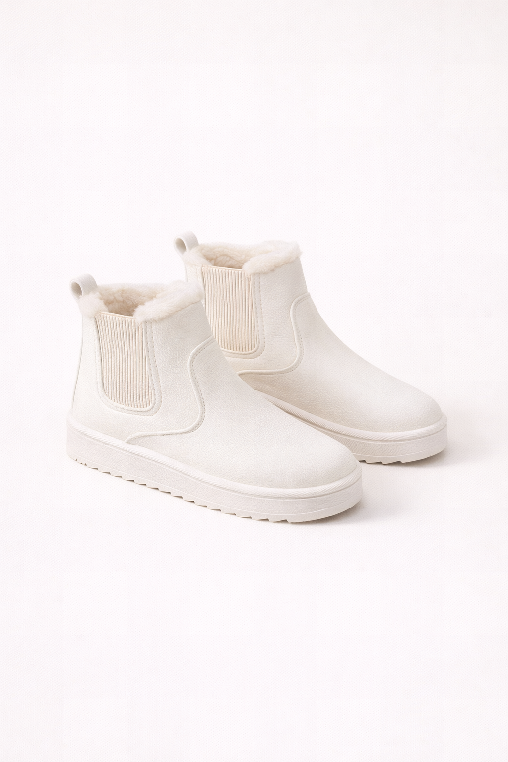 Witte gevoerde Chelsea boots met elastische zijkant en stevige zool gedragen door een vrouw op een houten vloer.